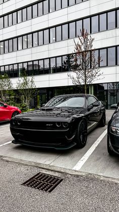 two black sports cars parked next to each other in a parking lot near a building