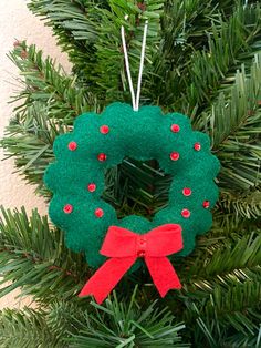 a green wreath ornament hanging from a christmas tree with red bows on it