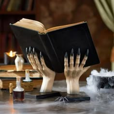 two hands holding an open book on top of a table with candles and other items