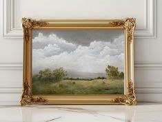 a painting hanging on the wall in front of a white wall with a gold frame