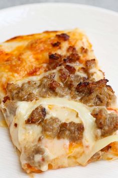 a piece of pizza with cheese and meat on it sitting on a white plate next to a fork