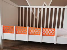 a white crib with three orange gates on the sides and a bed in the background