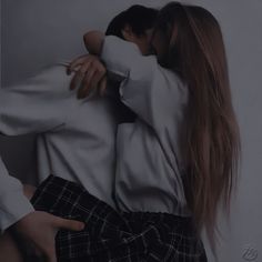 two people hugging each other in front of a white wall