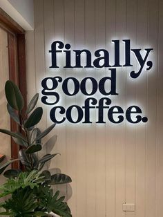 a sign that says finally, good coffee on the side of a wall next to a potted plant