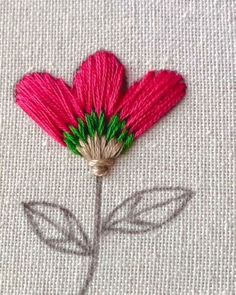 a pink flower with green leaves is on a piece of fabric that has been stitched together