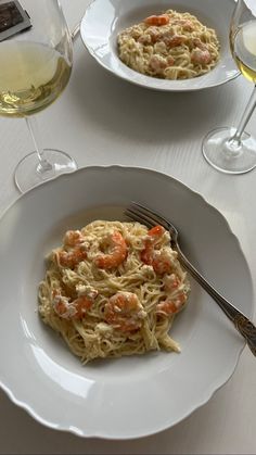 two white plates with pasta and shrimp on them next to some wine glasses filled with water