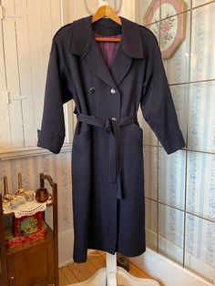 This sophisticated coat is made from heavier weight, 100 per cent pure virgin wool in classic navy blue. It has the original blue and gold buttons in the front and on the cuffs and shoulders; a matching tie belt and two front pockets, and is fully lined with thick purple blue satiny lining. The outside measurements, taken with the coat lying flat, are: shoulder to shoulder, 18 inches; armpit to armpit, 19 inches; sleeves, 23 inches; length, 49 inches; bottom edge, 30 inches. Please note that one of the front buttons is missing a bit of gold trim; also, the lining has some wear and discolouration at the bottom (see photos). Otherwise, the coat is in very good condition. Elegant Navy Peacoat With Double Button Closure, Elegant Navy Double-breasted Outerwear, Elegant Navy Pea Coat With Button Closure, Elegant Navy Double-breasted Peacoat, Navy Wool Peacoat For Office, Navy Elegant Wool Coat For Formal Occasions, Classic Long Navy Peacoat, Classic Navy Long Peacoat, Navy Classic Long Wool Coat