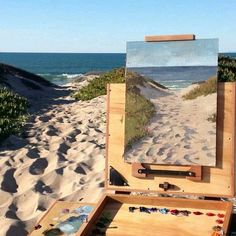 an artist's easel sitting on top of a sandy beach