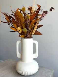 a white vase filled with lots of flowers on top of a table