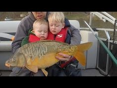 a man holding two children while sitting on a boat with a fish in his lap