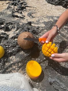 a person cutting mangos with a knife on top of the ground next to some fruit