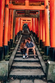 two people sitting on the steps in front of an orange building with columns and pillars