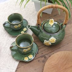 three green teapots with yellow flowers on them sitting next to a potted plant