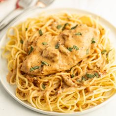 a white plate topped with pasta covered in gravy and meat sauce next to a fork