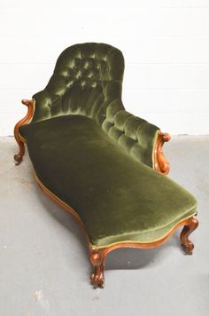 an old green velvet chaise lounge with wooden feet and arms, sitting on concrete floor