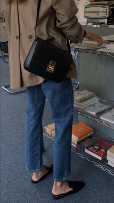 a woman standing in front of a bookshelf holding a black purse