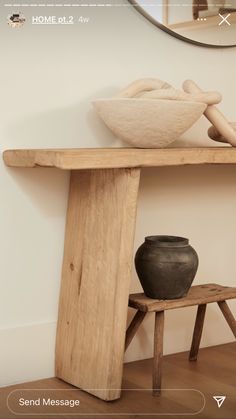 a wooden table with a bowl and vase on it next to a bench in front of a mirror