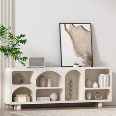 a white shelf with vases and other items on it next to a potted plant