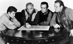 four men sitting around a table looking at a piece of paper