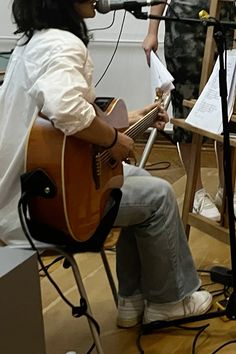 a woman sitting in front of a microphone while playing an acoustic guitar