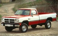 a red and white truck parked on top of a dirt road