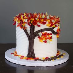 a white cake decorated with fall leaves and a tree on the top is sitting on a plate