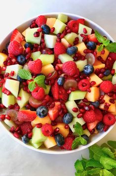 a white bowl filled with fruit salad on top of a table next to green leaves