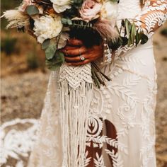 a woman in a white dress holding a bouquet of flowers and greenery on her arm