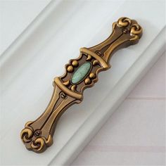 an ornate brass door handle with a green stone in the center on a white surface