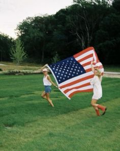 two girls running in the grass holding an american flag