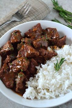 a white bowl filled with meat and rice on top of a table next to a fork