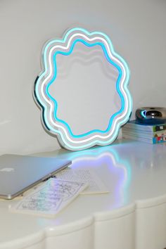 a laptop computer sitting on top of a white table next to a neon light mirror