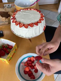 a person cutting strawberries on top of a cake