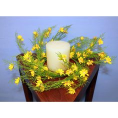 a white candle sitting on top of a wooden table filled with yellow flowers and greenery