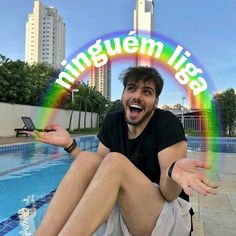 a man sitting on the edge of a swimming pool in front of a rainbow sign