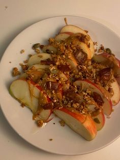 a white plate topped with sliced apples and granola toppings on top of it