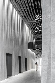 a woman walking down a long hallway with columns and numbers on the wall behind her