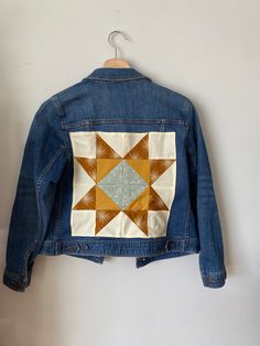 a denim jacket hanging on a wall with an orange and blue patchwork design in the back