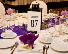 the table is set with white plates and silverware, purple napkins and flowers