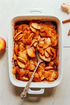 a casserole dish filled with sliced apples and cinnamon sticks next to an apple