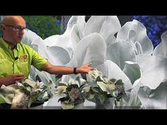 a man standing in front of a large white flower with his hands out to the side