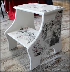 a white step stool with floral designs painted on the front and sides, sitting on a wooden floor