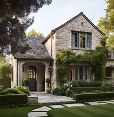 a house that is in the middle of some grass and bushes with trees around it