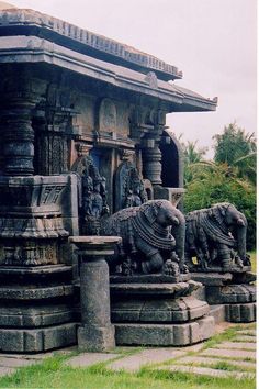 some statues on the side of a building with grass and trees in the foreground