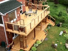 a large deck with chairs and tables in the middle of a garden area next to a brick building