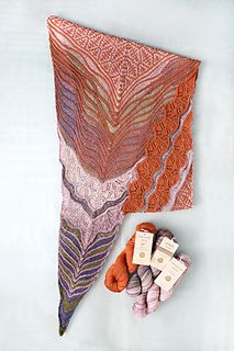 an orange and purple shawl next to some crocheted items on a white surface