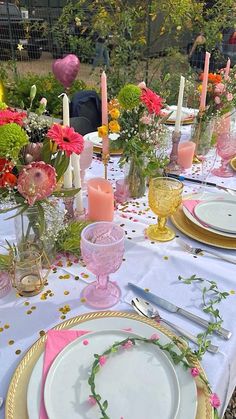 the table is set with pink and yellow flowers in vases, candles, and plates