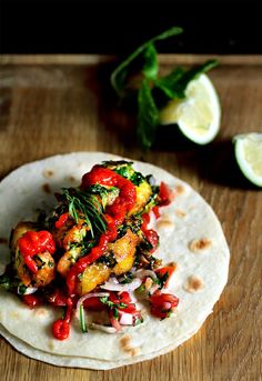 a tortilla topped with chicken and vegetables on a wooden table next to lime wedges