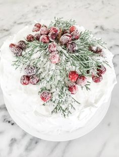 a frosted cake topped with cranberries and evergreen sprigs