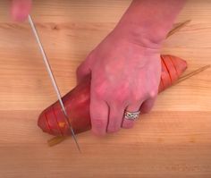 a person holding a knife and cutting up a piece of food on a wooden table